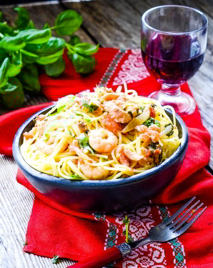 long shot of bowl of seafood pasta with red wine glass behind