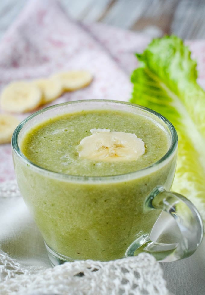 smoothie in cup with lettuce leaf behind and slice of banana on top