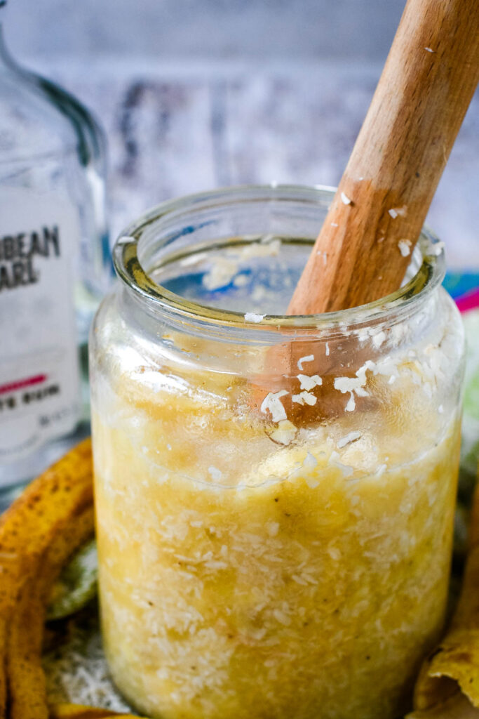 all ingredients for homemade tropical liqueur in jar with pestle