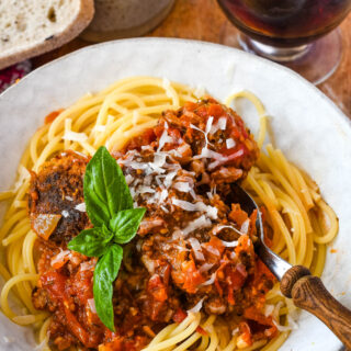 vegan meatballs in tomato sauce with spaghetti on plate with glass of red wine behind