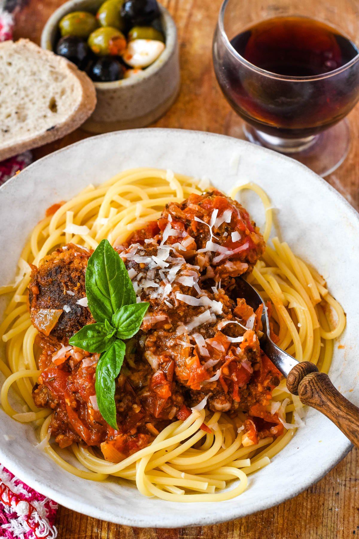 vegan meatballs in tomato sauce with spaghetti on plate with glass of red wine behind