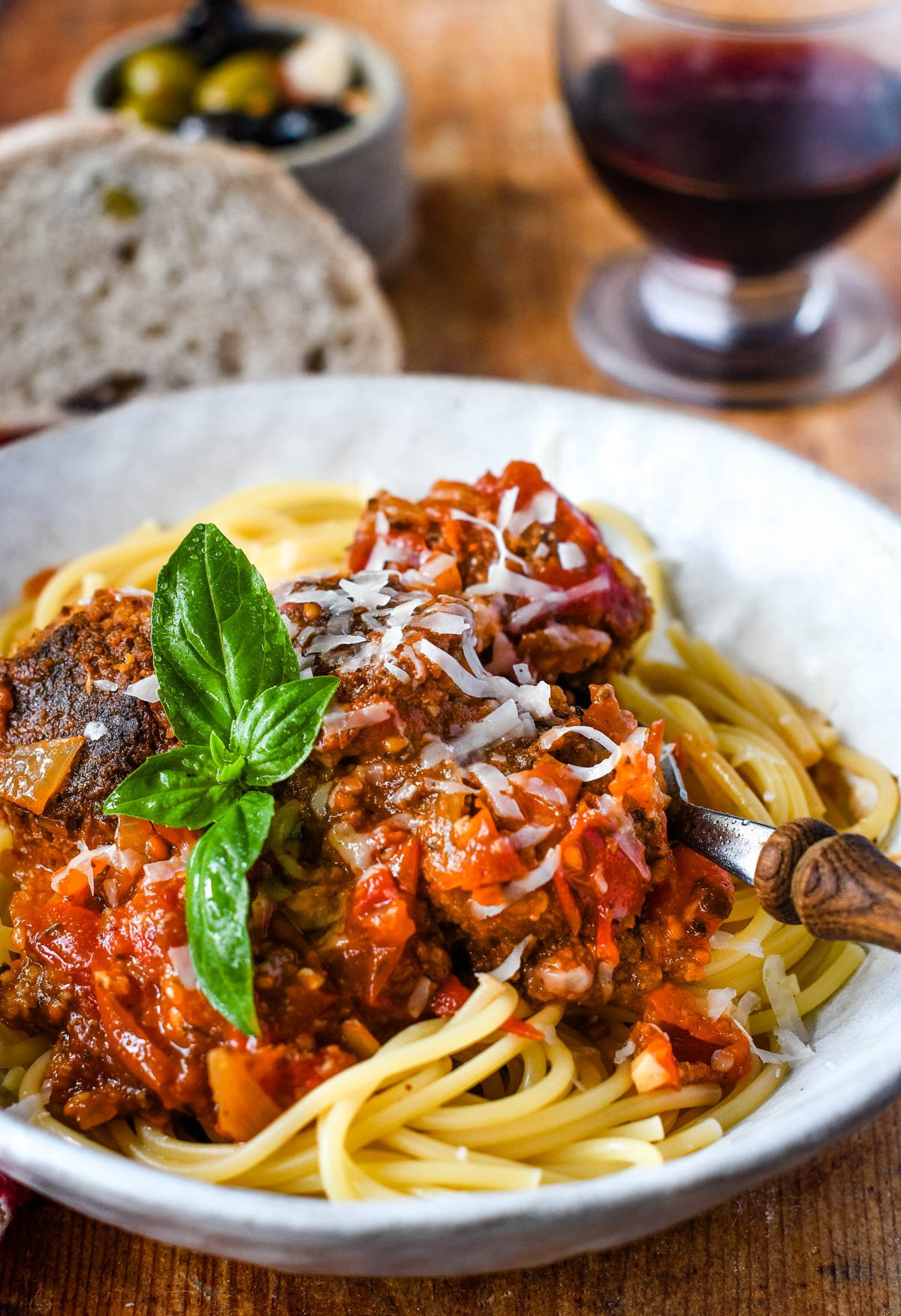 vegan meatballs in tomato sauce with spaghetti on plate with red wine and bread behind