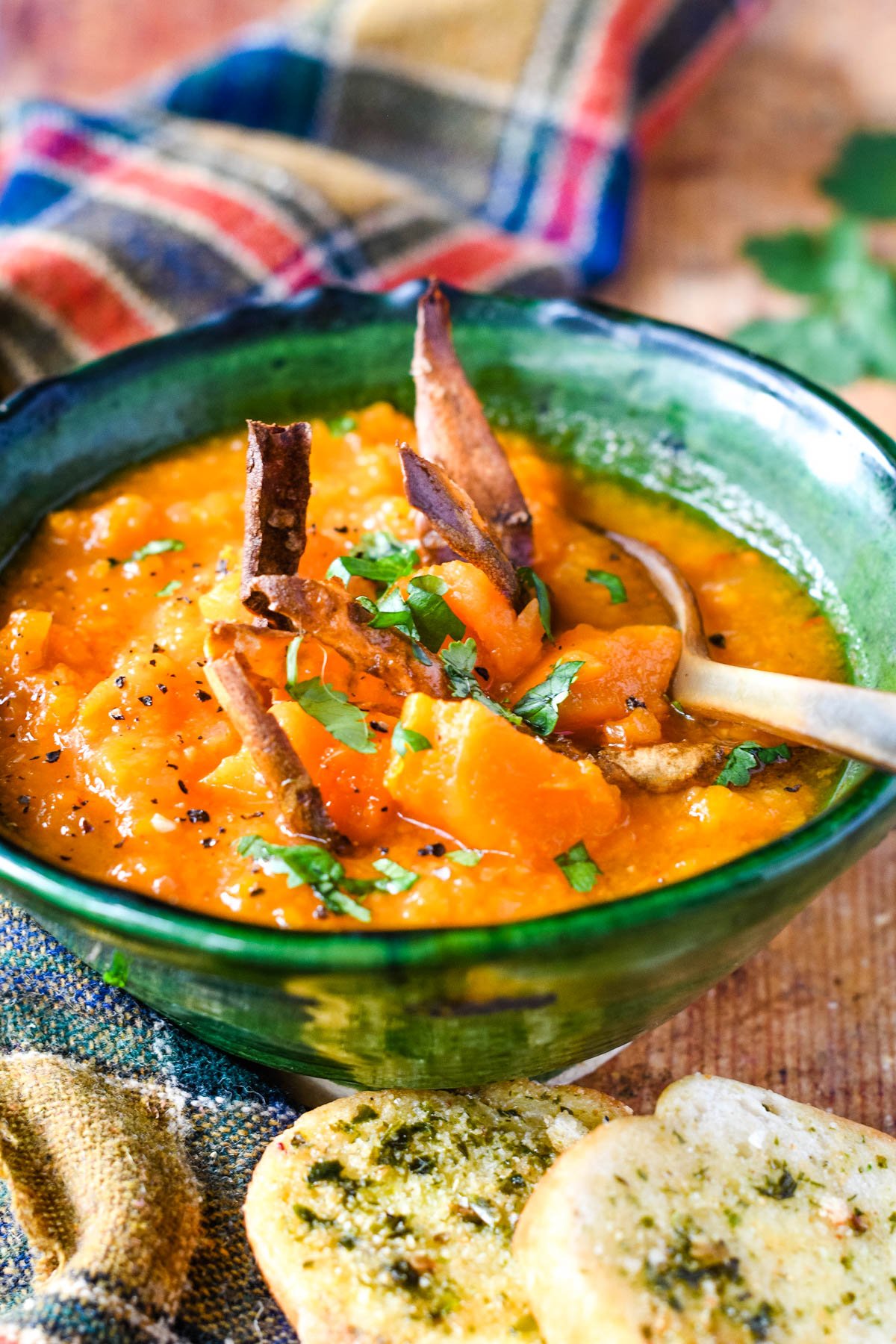 green bowl of sweet potato soup with spoon in it and bread at the side