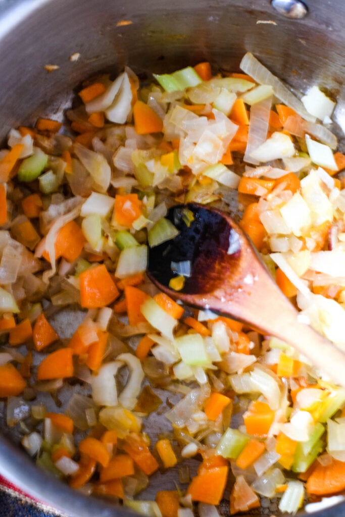 sauteing the carrot, celery and garlic in pan with wooden spoon