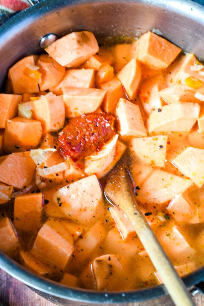 sweet potato cubes and harissa paste in pan with wooden spoon