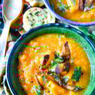 top down shot of sweet potato soup with second bowl, spoons and bread on table