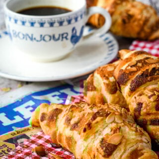 three homemade almond croissants beside a cup of coffee and red and white napkin