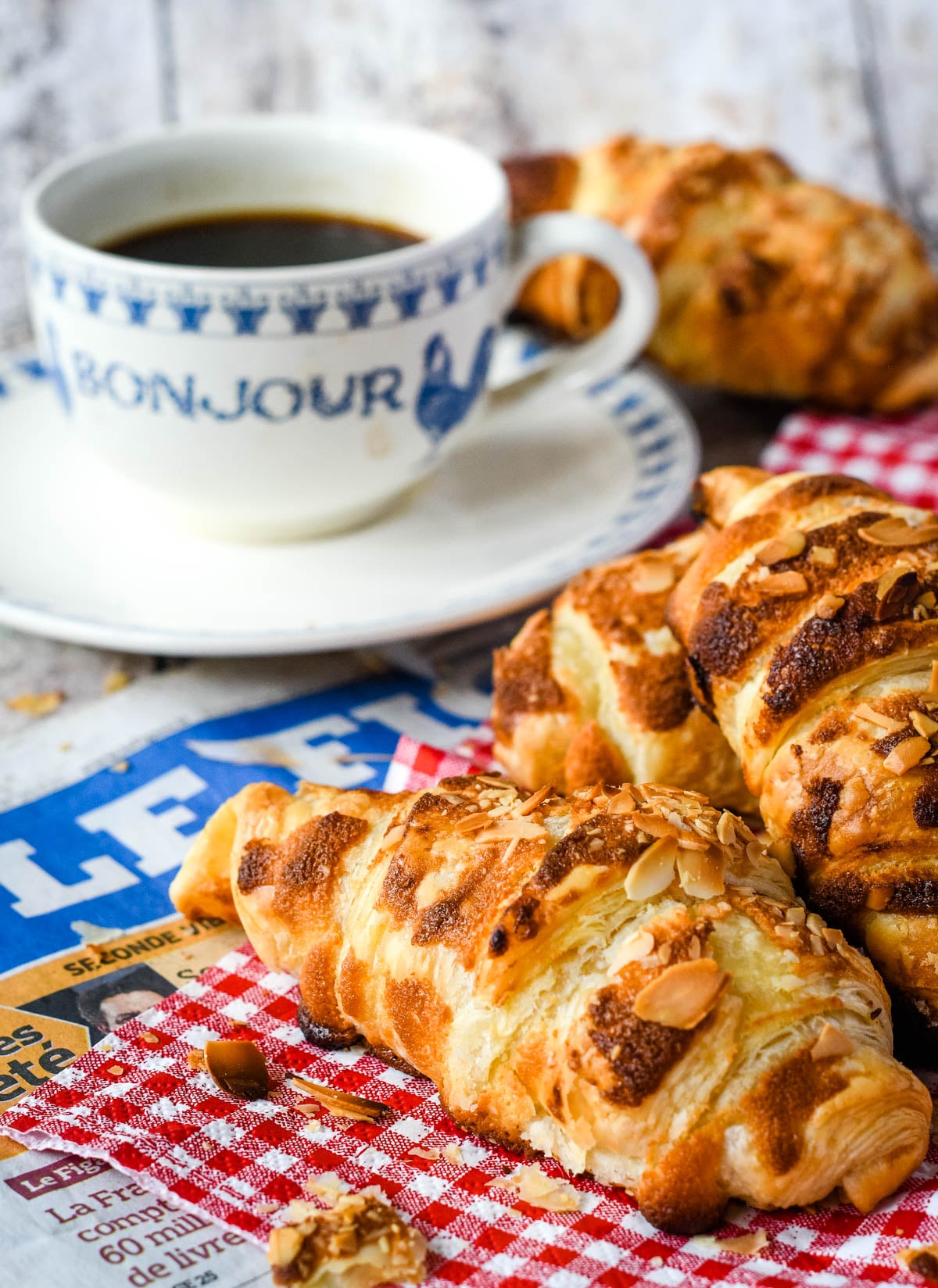 three homemade almond croissants beside a cup of coffee and red and white napkin