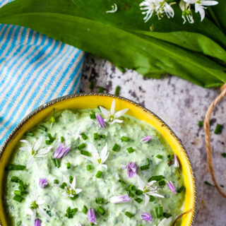 top down shot of bowl of wild garlic dip with wild garlic leaves and flowers above