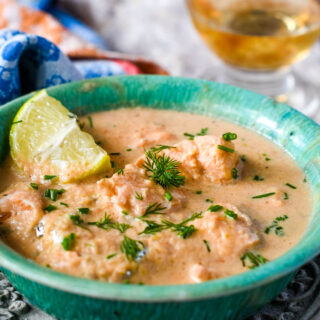 blue bowl of salmon soup with slice of lemon, glass of wine behind