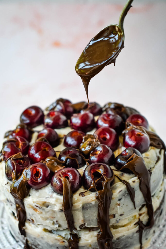 drizzling melted chocolate on top of the cherry topped cake
