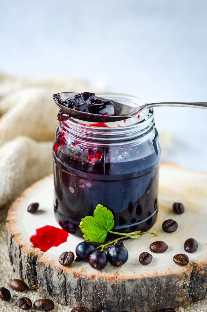 jar of blackcurrant coffee jelly on bood base with spoon on top