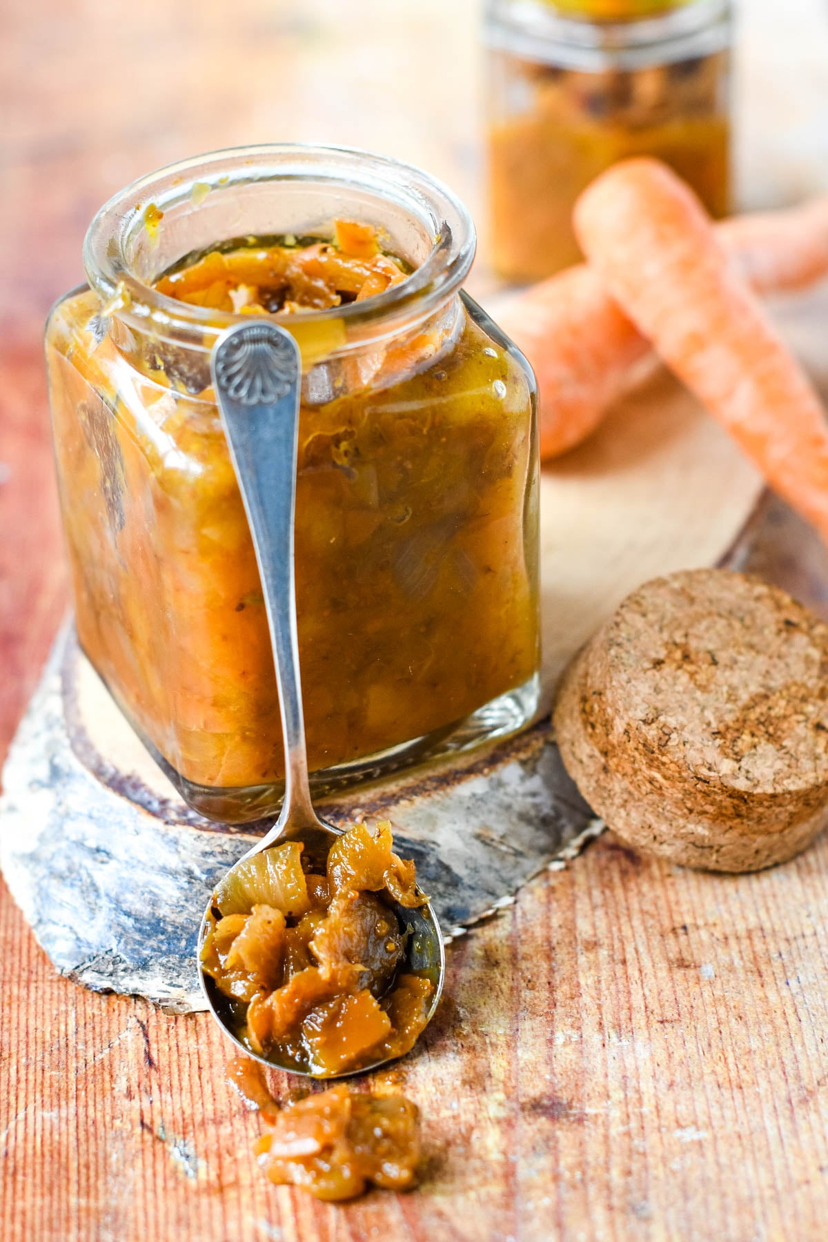jar of carrot peel chutney with spoon and carrots behind