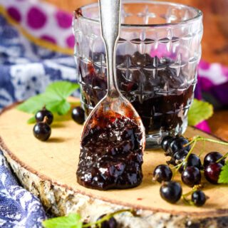 Blackcurrant chutney in jar on log with blackcurrants