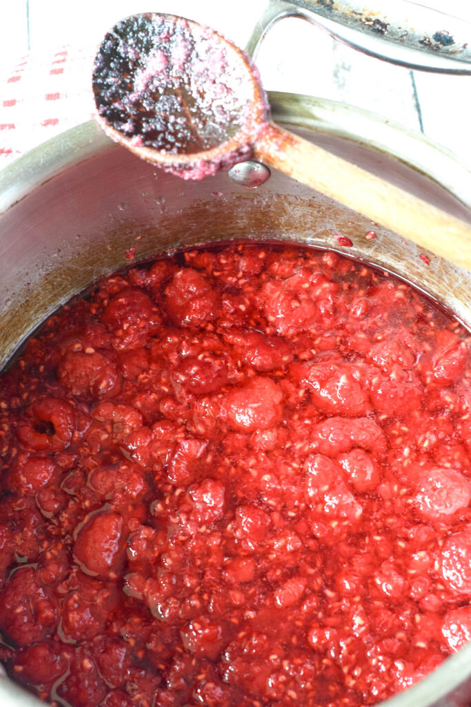 raspberry jam in pan with wooden spoon