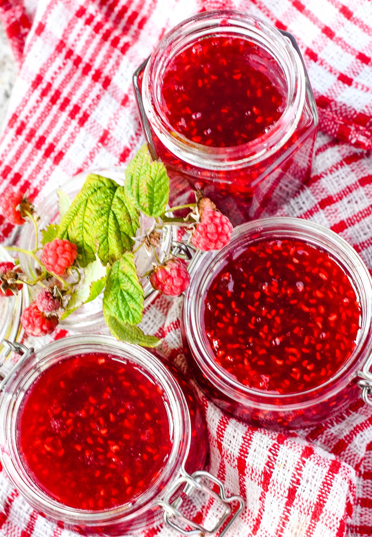 three jars of raspberry jam on checked table cloth