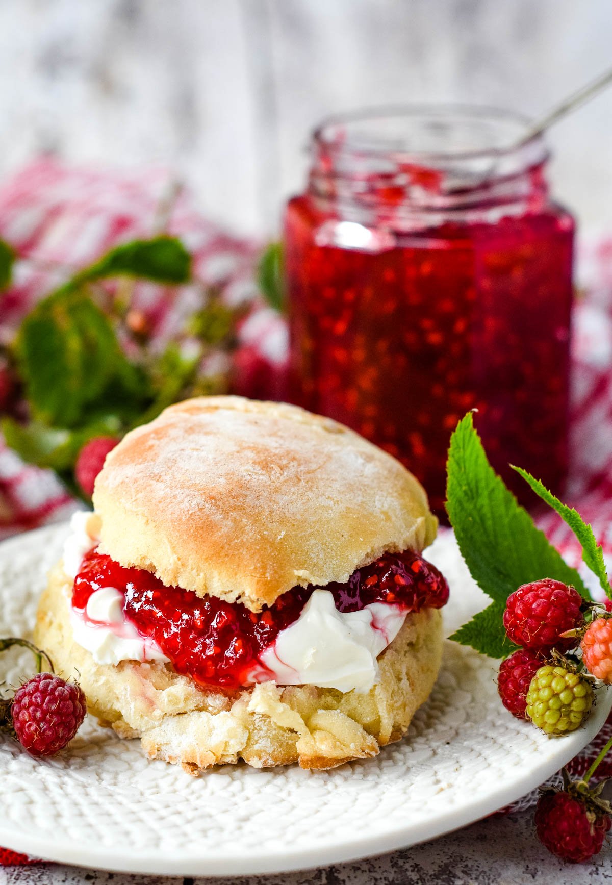 raspberry jam on a scone with cream and jar of jam behind