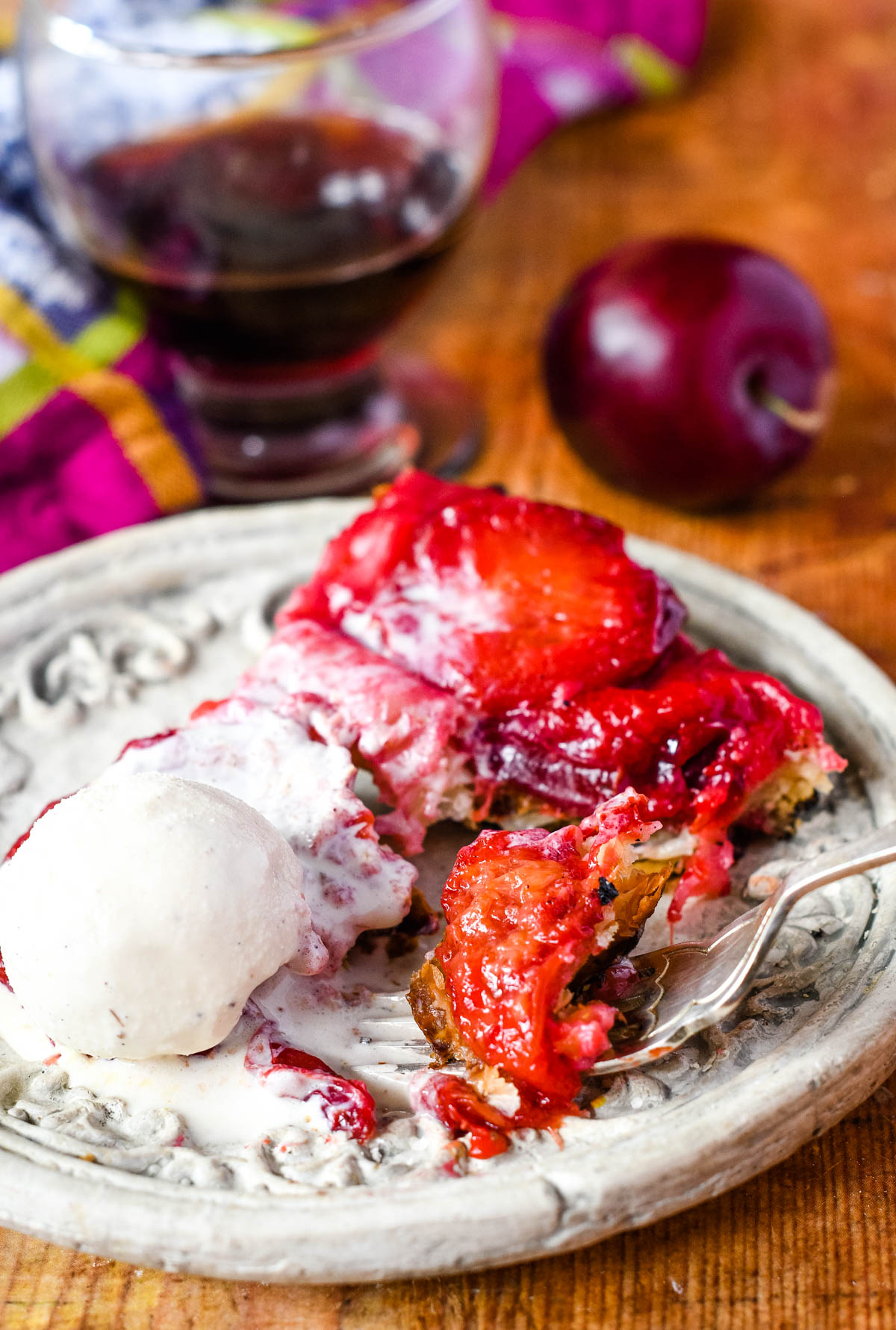 plum tarte tatin on a plate with ice cream and a fork of pie being lifted off