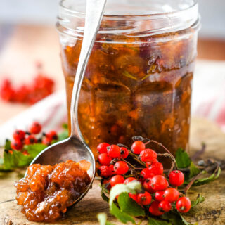 rowan berry chutney in jar with spoon beside and rowan berries and leaves