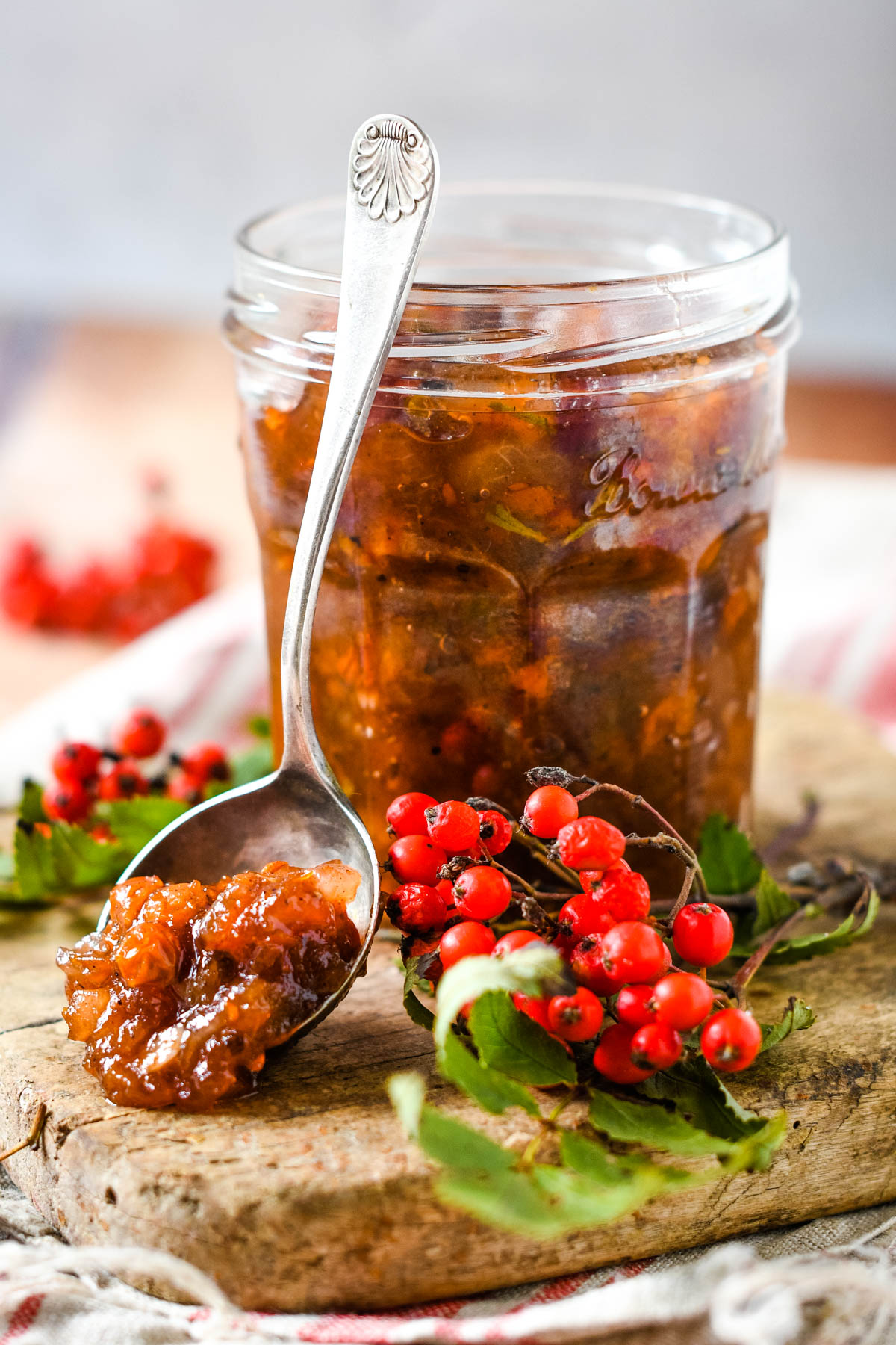rowan berry chutney in jar with spoon beside and rowan berries and leaves