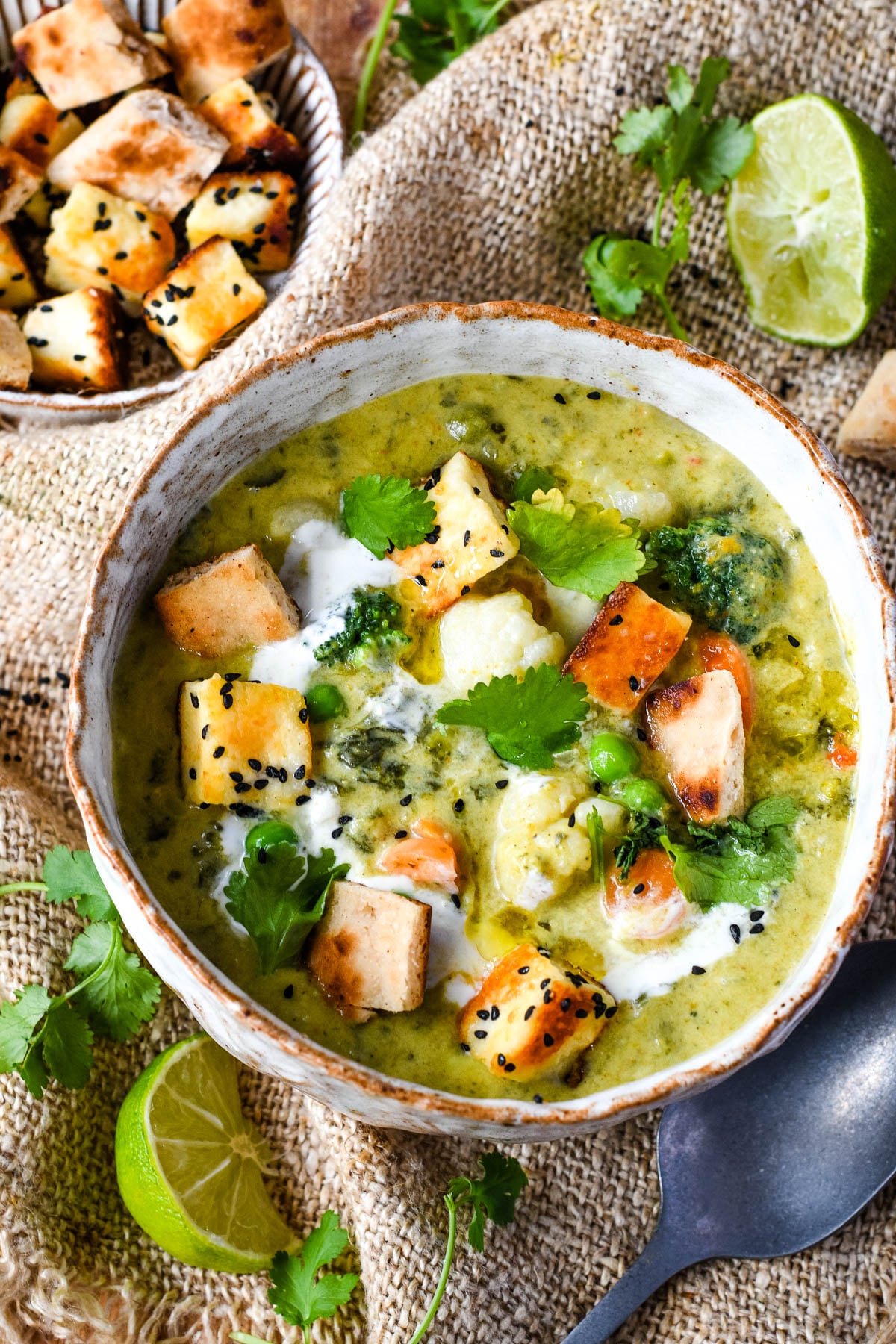 top down shot of curry vegetable soup with croutons and limes
