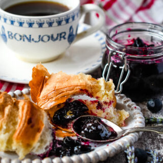 blueberry jam on croissant with coffee and jar behind
