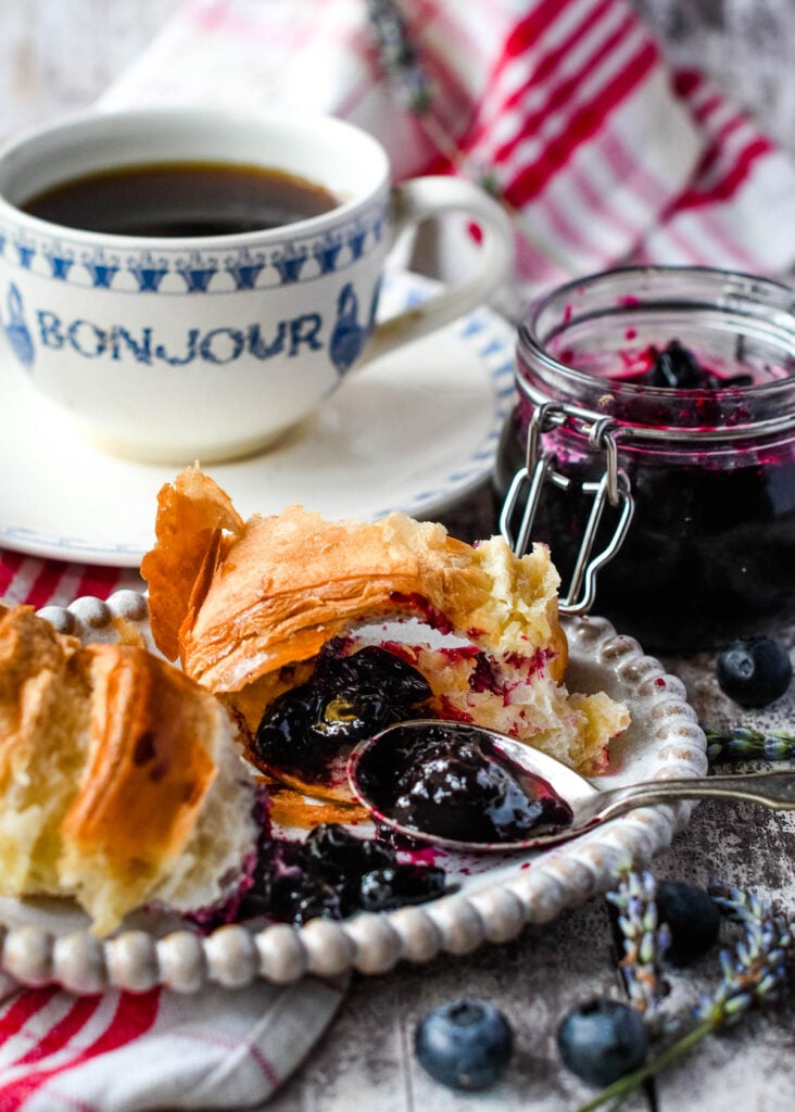 blueberry jam on croissant with coffee and jar behind