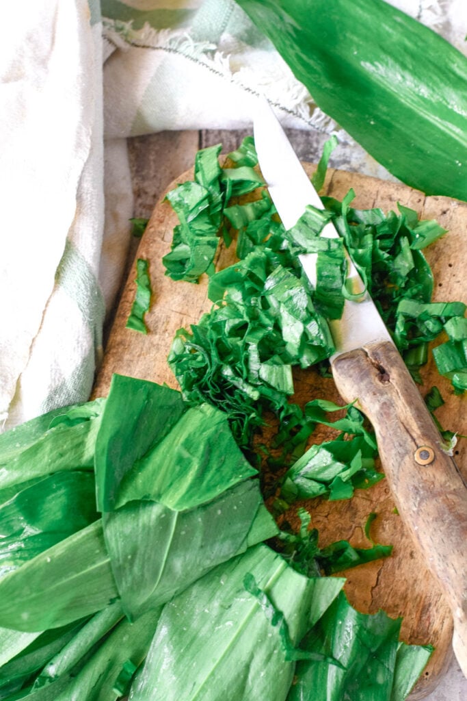 chopping the wild garlic leaves on old wooden board with knife