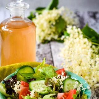 Elderflower vinegar with salad in front and flowers at side