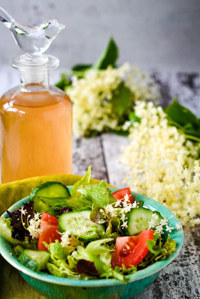 Elderflower vinegar with salad in front and flowers at side