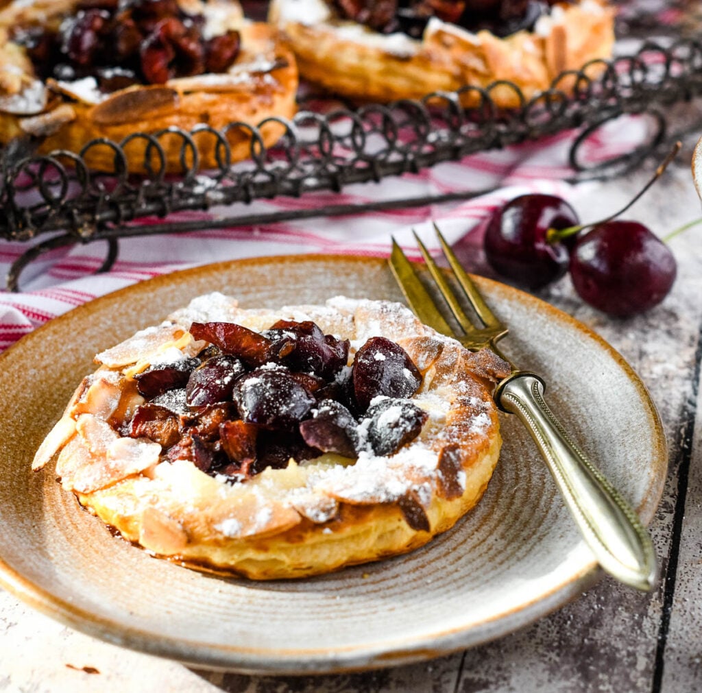 close up of cherry puff tart on plate with fork