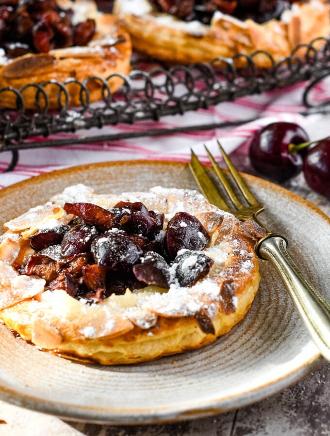 close up of cherry puff tart on plate with fork