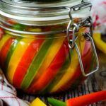 finished jar of mixed pickled peppers with a few slices beside the jar