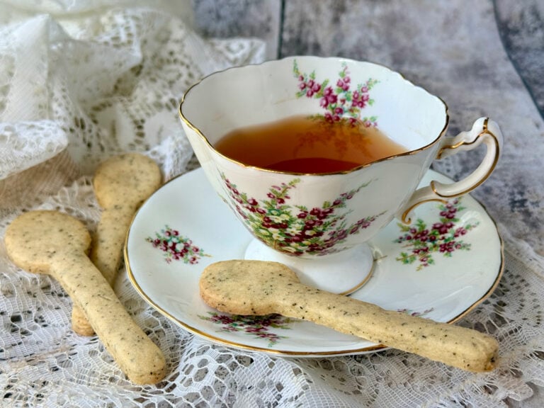 Vintage floral teacup with tea served beside spoon-shaped biscuits on a lace tablecloth.
