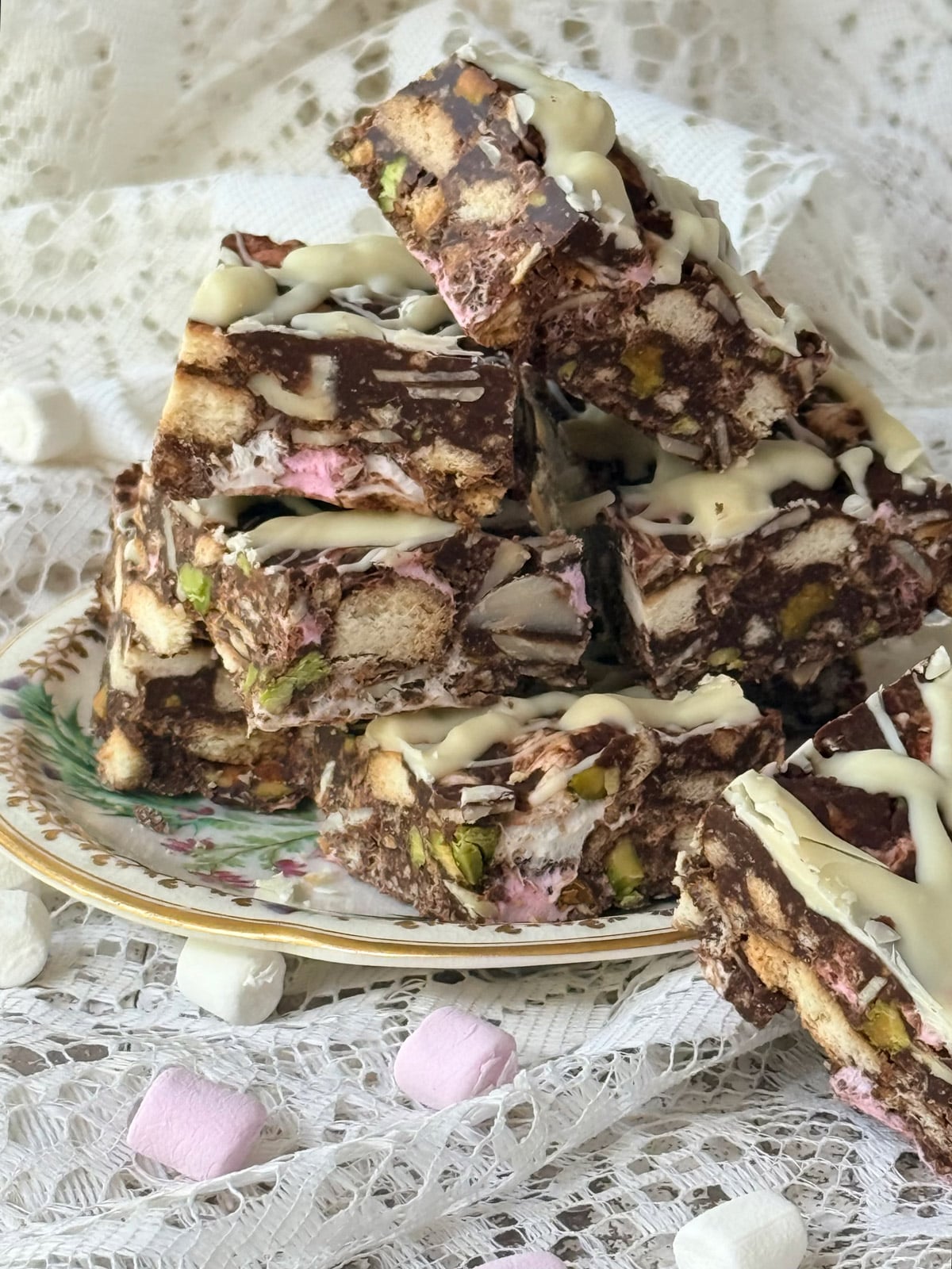 Chocolate rocky road pieces with marshmallows, biscuits, pistachios, and white chocolate drizzle.