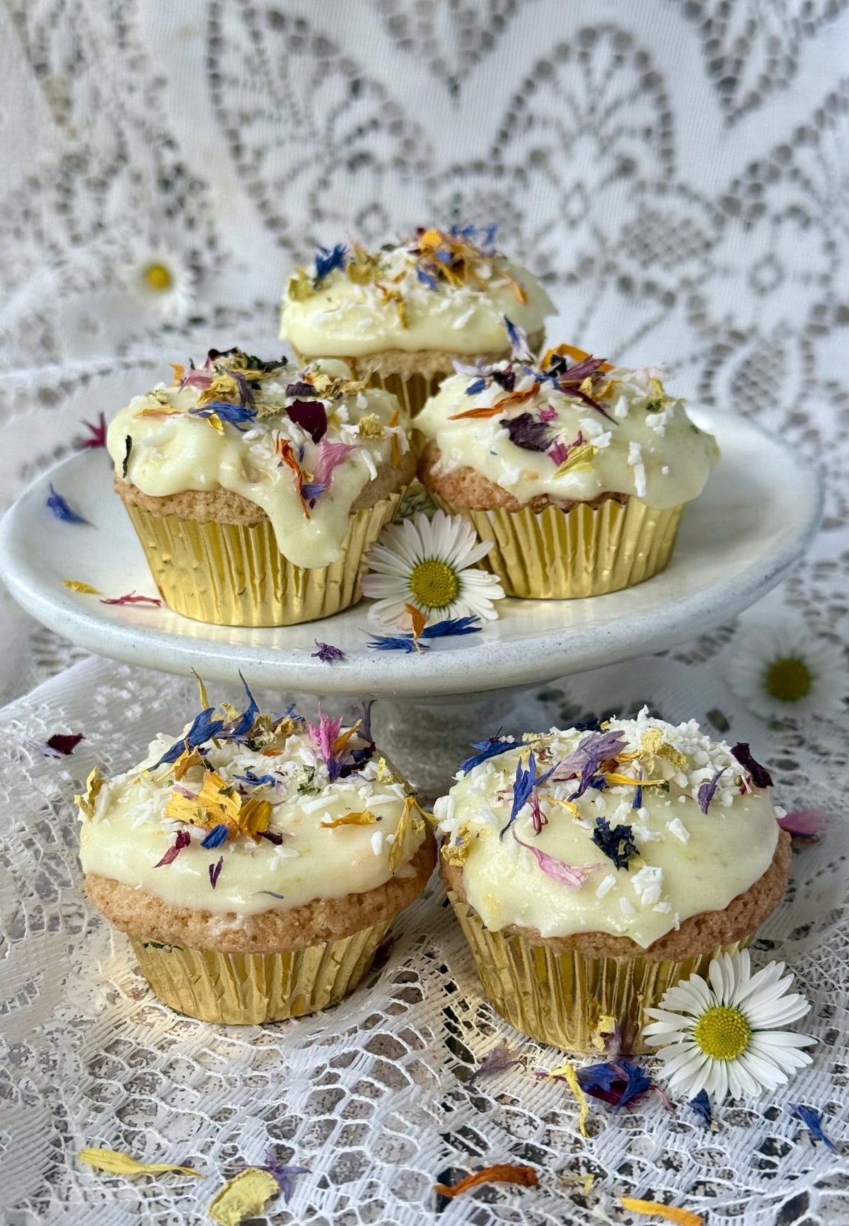 Small frosted cakes in gold cases topped with dried edible flowers and coconut.