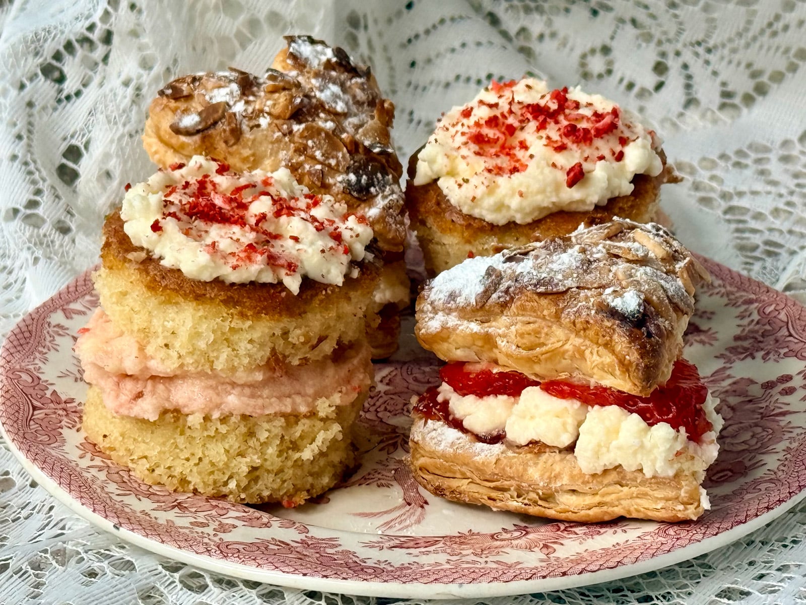 Sweet afternoon tea pastries and mini cakes filled with cream and fruit on a floral plate.