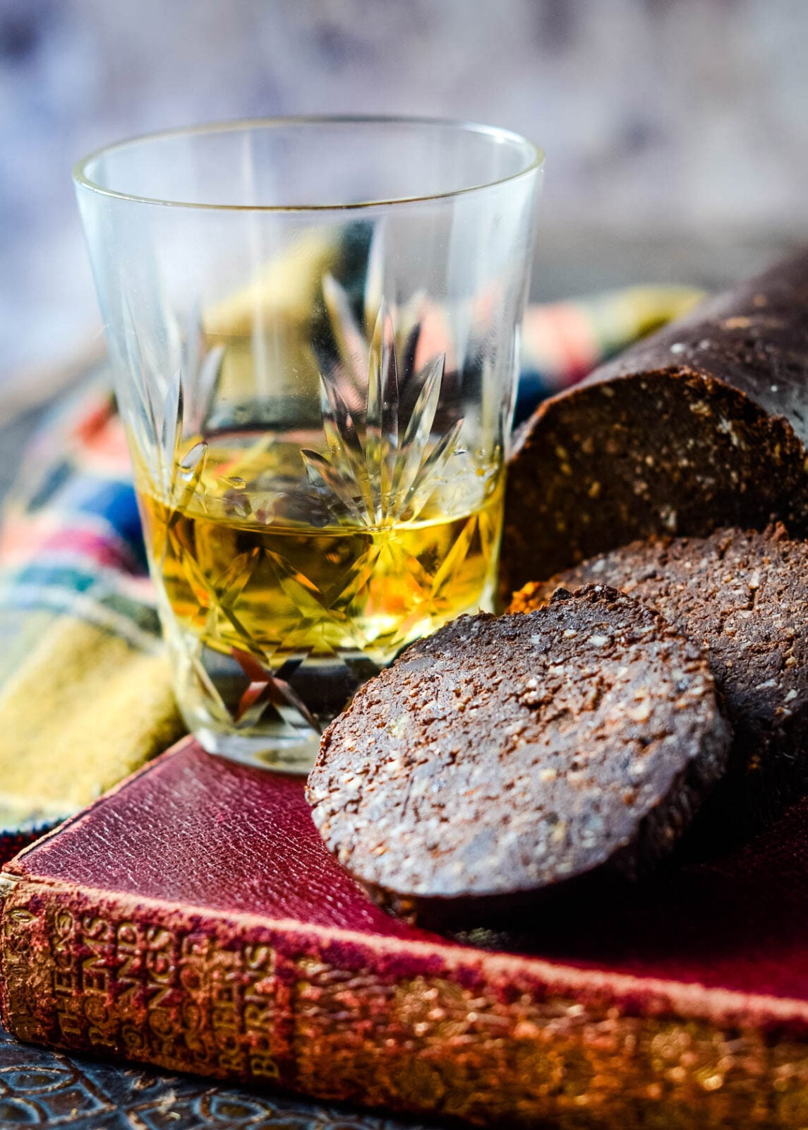 Sliced chocolate haggis served beside a glass of whisky on a vintage book.