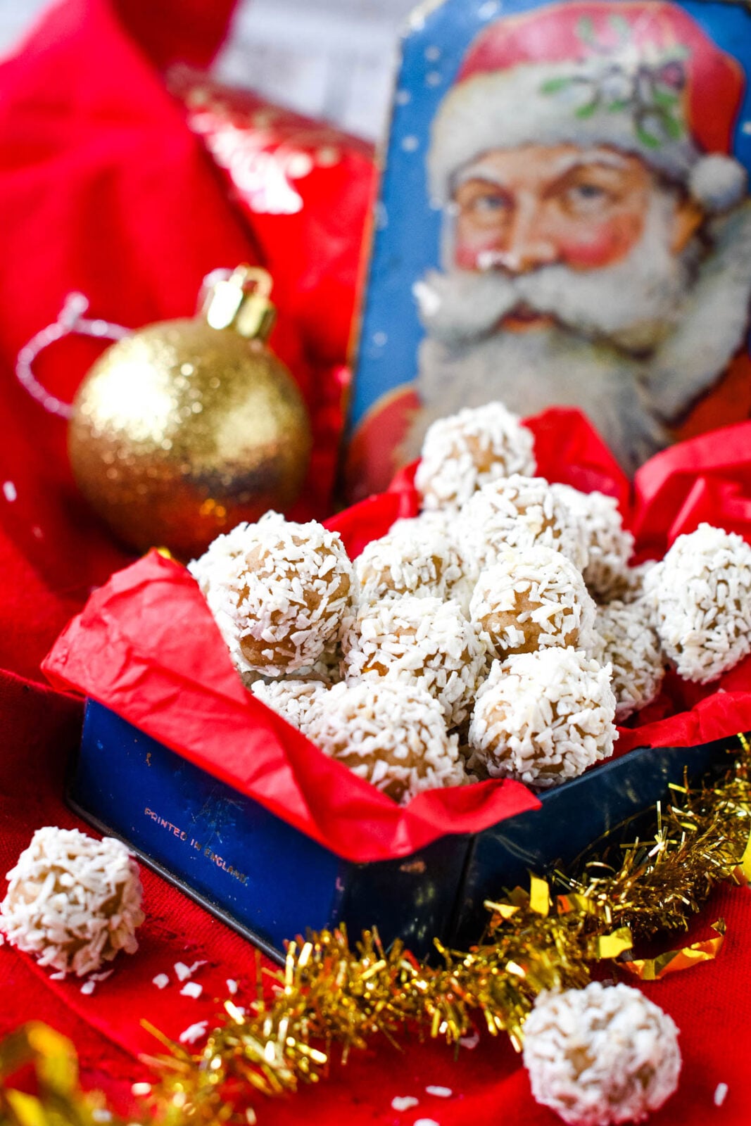 Christmas pudding snowballs coated in coconut and arranged in a festive tin with Christmas decorations.