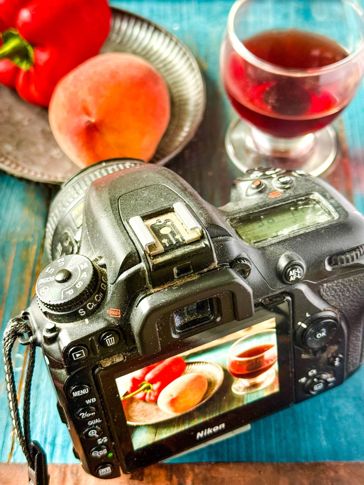 DSLR camera photographing a styled food scene with a peach, red pepper, and glass of red wine.
