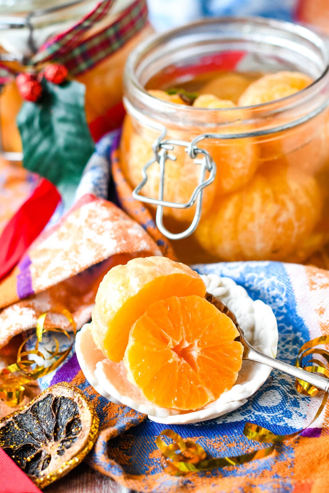 Clementines preserved in brandy in a glass jar with fresh clementine segments and festive ribbons.