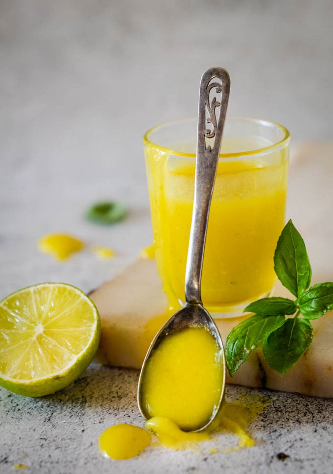 Homemade lime curd with basil in a glass, served with a spoonful of curd, fresh lime, and basil leaves.