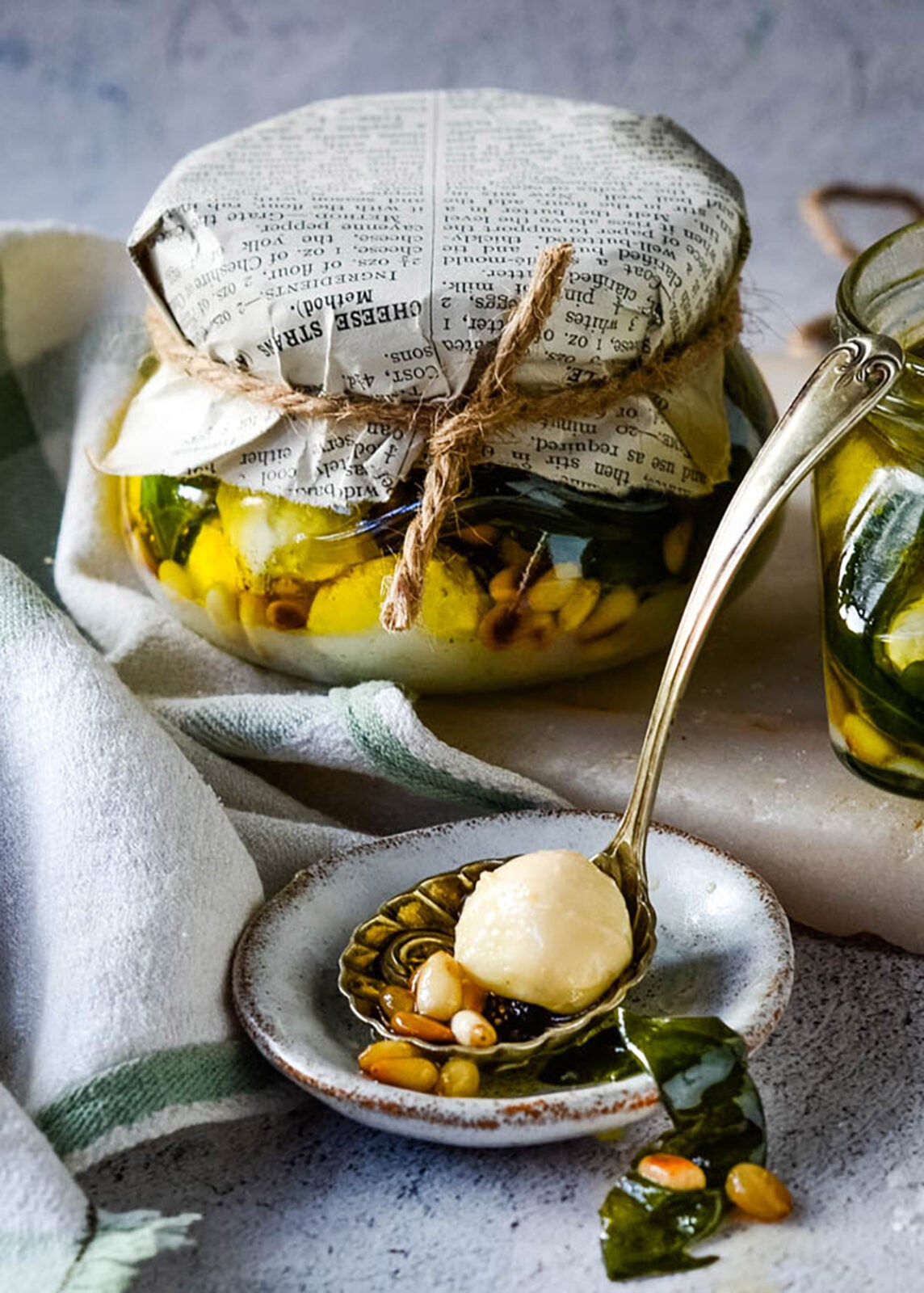 Pesto mozzarella balls preserved in oil with pine nuts and basil, served from a small glass jar.